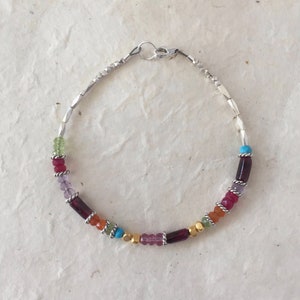 May include: A silver bracelet with a clasp closure and a variety of colorful gemstones, including green, red, orange, purple, and turquoise.