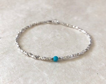 May include: A delicate silver bracelet with a single turquoise bead. The bracelet is made of small, faceted beads and has a simple clasp.