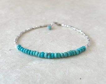 May include: A delicate silver bracelet with a row of turquoise beads.