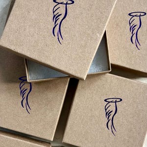 Pode incluir: V&aacute;rias caixas de cart&atilde;o castanho com um desenho de asa de anjo azul no topo de cada caixa.