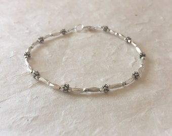 Puede incluir: Un brazalete de plata con pequeños abalorios en forma de flor. El brazalete está hecho de metal martillado y tiene un diseño sencillo.