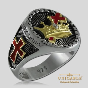 Könnte beinhalten: Ein silberner Ring mit einem schwarzen und goldenen Design, das eine Krone und ein rotes Kreuz zeigt. Der Ring ist mit den Worten "In Hoc Signo" und "925" beschriftet.