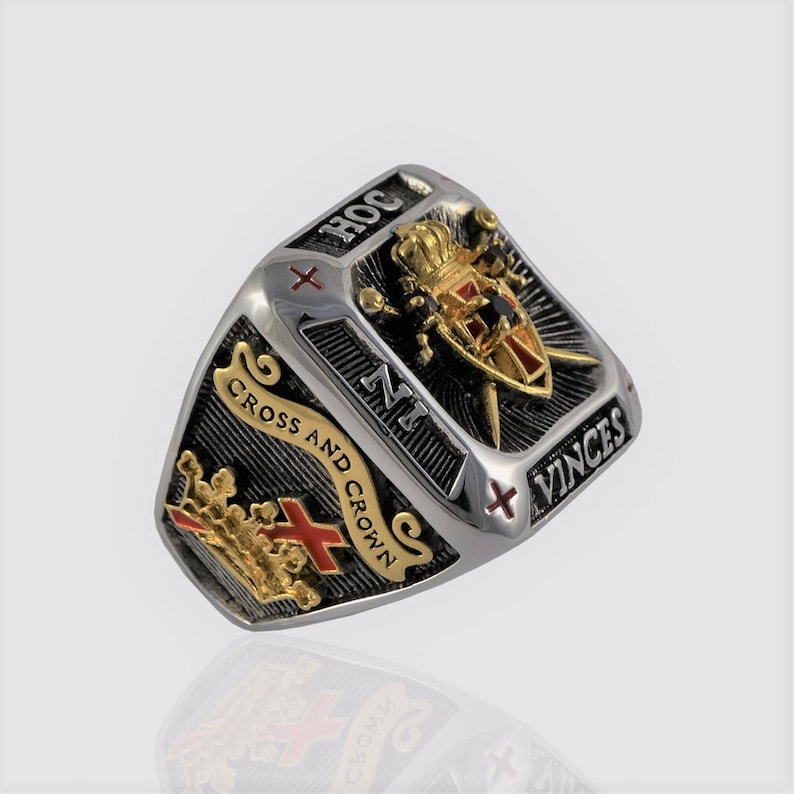 Puede incluir: Un anillo de plata y negro con un escudo dorado que presenta una cruz, una corona y espadas. El escudo est&aacute; rodeado por el texto "HOC  NI  VINCES" y "CROSS AND CROWN".