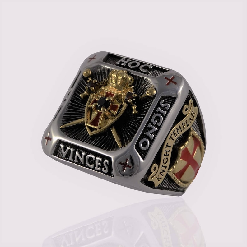 Puede incluir: Un anillo de plata y oro con un dise&ntilde;o de escudo negro y dorado. El escudo tiene una cruz roja y una piedra negra en el centro. El anillo tambi&eacute;n tiene las palabras "Hoc Signo Vinces" y "Caballero Templario" inscritas en &eacute;l.