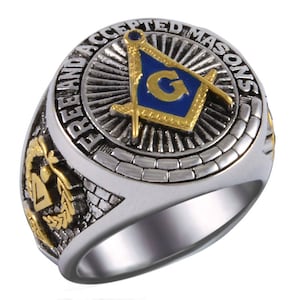 May include: A silver-toned ring with gold and blue Masonic symbols. The ring features the words "FREE AND ACCEPTED MASONS" around the central emblem. The design includes a compass and square, with a "G" in the center, and additional gold accents.