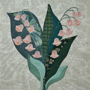 May include: A close-up of a fabric art piece depicting a bouquet of lily of the valley flowers. The flowers are pink and the leaves are green. The background is a light beige fabric with a floral pattern.