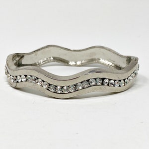 May include: A silver bangle bracelet with a wavy design and a row of clear rhinestones.