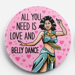 May include: A pink button with a white outline and a white heart pattern. The button features a cartoon illustration of a woman in a blue and gold belly dancing costume. The text "All you need is love and belly dance" is written in black.