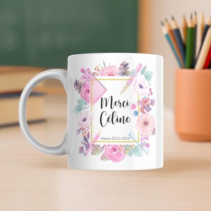 May include: White ceramic mug featuring a floral design with pink and purple flowers, a pink pencil, and the text "Merci C&eacute;line". The mug also includes the text "Hamza 2023-2024" in a gold frame.