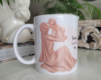May include: White ceramic mug with a pink illustration of a woman in a headscarf holding a baby. The text "Inaya 02-08-2021" is printed on the mug.