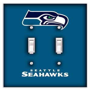 May include: A light blue and white light switch cover with the Seattle Seahawks logo and the words "Seattle Seahawks" in white text.