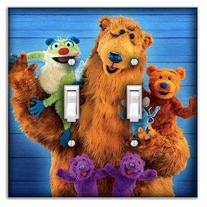 May include: A light blue double light switch plate featuring a colorful illustration of the characters from the children's television show "Bear in the Big Blue House". The characters include Bear, Tutter, and Ojo. The characters are smiling and appear to be singing.