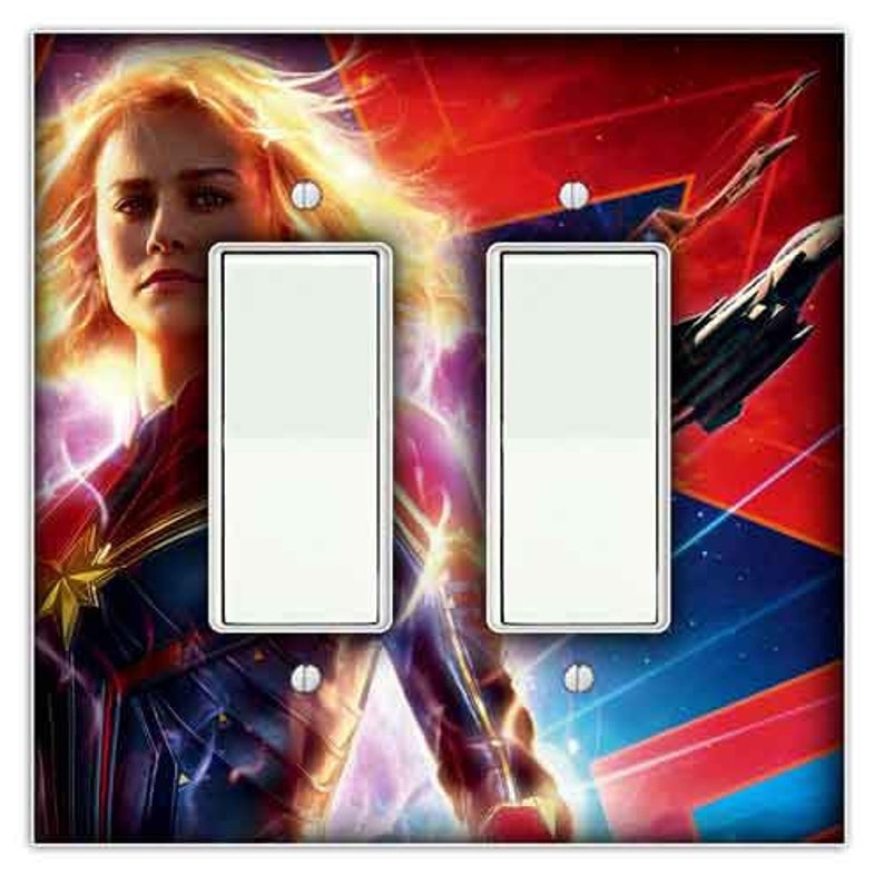 May include: A double light switch plate featuring a colourful image of Captain Marvel, a superhero from the Marvel Cinematic Universe. The image shows Captain Marvel in a red, blue, and gold costume, with a glowing energy effect around her. The background is a mix of red, blue, and purple colours.