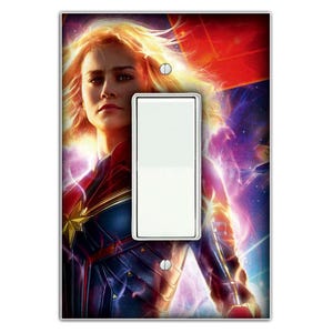 May include: A light switch cover featuring a colourful image of Captain Marvel, a superhero from the Marvel Cinematic Universe. The image shows Captain Marvel in a blue and red costume, with a glowing energy effect behind her. The switch cover is designed to fit standard light switches.