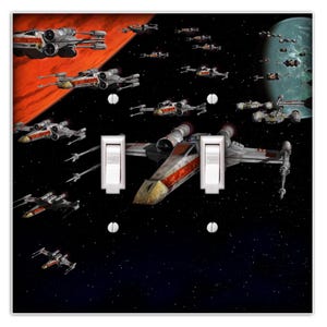 May include: A light switch cover featuring a Star Wars X-Wing fighter squadron flying through space. The cover has a black background with a red and orange nebula in the upper left corner. The X-Wings are flying in formation, with a large X-Wing in the center of the image. The cover has two toggle switches.