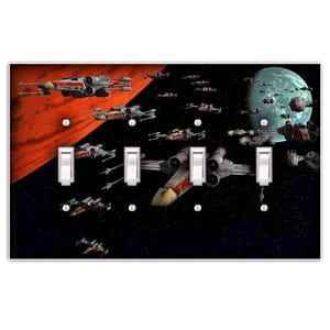 May include: A light switch plate featuring a space scene with a red planet, a green planet, and a fleet of X-Wing starfighters flying in formation. The switch plate has three toggle switches.