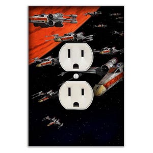 May include: A black and red wall plate with two standard electrical outlets. The plate features a design of X-Wing starfighters from the Star Wars franchise flying through space.