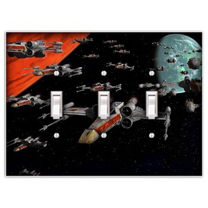 May include: A light switch plate featuring a Star Wars themed design with X-Wing fighters flying through space. The background is a dark blue with stars and a red planet. The switch plate has three toggle switches.