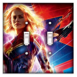May include: A light switch plate featuring a colourful image of Captain Marvel, a superhero from the Marvel Cinematic Universe. The image shows Captain Marvel in a blue and red costume, with her hair flowing behind her. The background is a dark blue space scene with stars and a red and orange nebula.