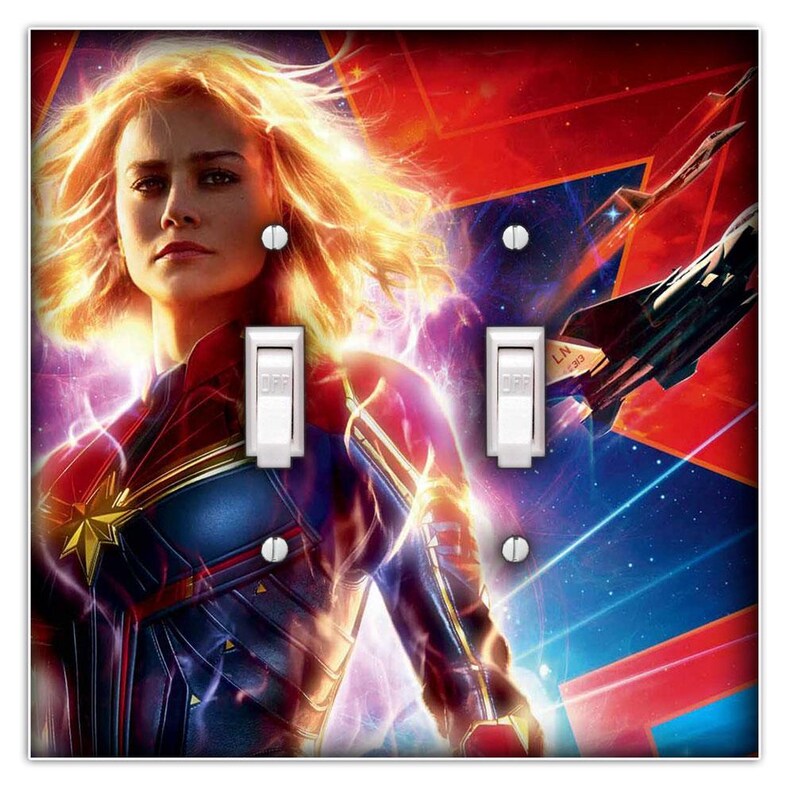 May include: A light switch plate featuring a colourful image of Captain Marvel, a superhero from the Marvel Cinematic Universe. The image shows Captain Marvel in a blue and red costume, with her hair flowing behind her. The background is a dark blue space scene with stars and a red and orange nebula.
