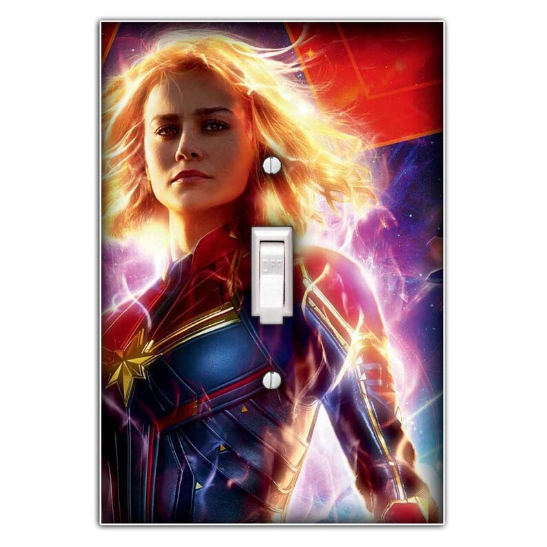 May include: A light switch cover featuring a colourful image of Captain Marvel, a superhero from the Marvel Cinematic Universe. She is wearing her signature red, blue and gold costume and has a determined expression on her face. The background is a swirling nebula of purple, pink and blue.