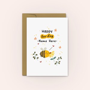 Peut inclure: Une carte blanche avec une illustration de dessin anim&eacute; d'une abeille jaune et le texte "Happy bee-day -Name Here- ". L'abeille tient une fleur jaune et a une expression joyeuse. La carte est entour&eacute;e de petites fleurs et de c&oelig;urs.