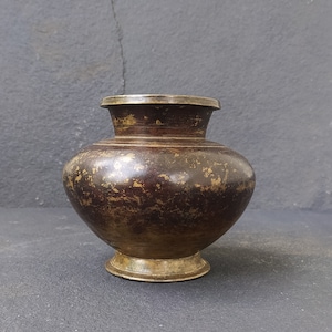 May include: A small, antique brass vase with a rounded body and a flared lip. The vase has a dark brown patina and shows signs of age.