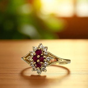May include: A gold ring featuring a cluster of small, round, deep red gemstones surrounded by smaller, clear gemstones. The ring has a decorative, openwork design on the band and a diamond-shaped setting.