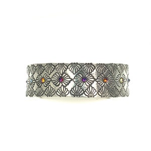 May include: A silver bracelet with a floral design and colorful gemstones. The bracelet is made of metal and has a textured surface.