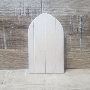 Könnte beinhalten: Eine einfache, unfertige Holztür mit einem spitzen Bogen oben. Die Tür besteht aus dünnen Holzbrettern und hat eine helle Holzfarbe.