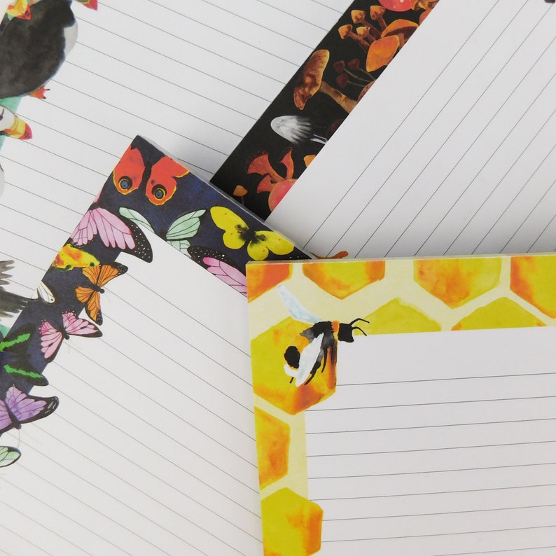 May include: Three different lined notepads with colourful illustrations. The first notepad has a black background with colourful butterflies and a bee. The second notepad has a black background with mushrooms and a white background with a bee. The third notepad has a yellow honeycomb background with a bee.