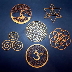 Könnte beinhalten: Sechs Holz-Wanddekorationen mit verschiedenen spirituellen und geometrischen Designs. Die Designs umfassen einen Lebensbaum, eine Lebensblume, eine dreifache Spirale, einen Lebenssamen, einen Davidstern und ein Om-Symbol.