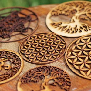 May include: Six wooden coasters featuring intricate laser-cut designs. The designs include a flower of life, a tree of life, and an Om symbol.
