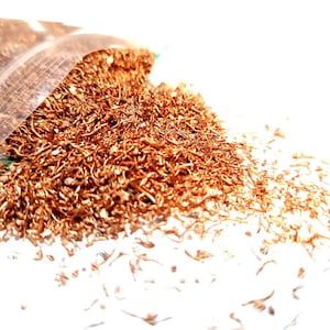 May include: A close-up of a pile of copper wire scrap. The wire is thin and tangled, and it is a bright orange-brown color. The scrap is spilling out of a clear plastic bag.