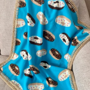 May include: A blue fleece blanket with a donut pattern. The blanket has a crocheted border in a tan color.