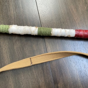 May include: A brown leather strap with a green, white and red striped handle. The handle is wrapped in fabric and leather.