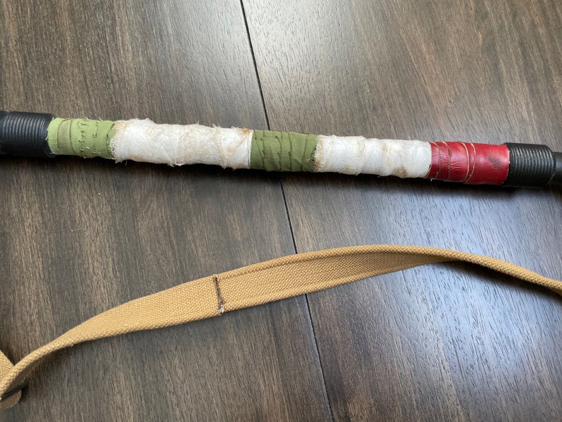 May include: A brown leather strap with a green, white and red striped handle. The handle is wrapped in fabric and leather.