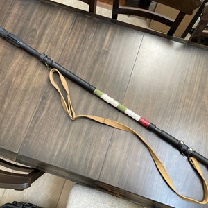 May include: A black walking stick with a brown leather strap and a green, white and red striped section.