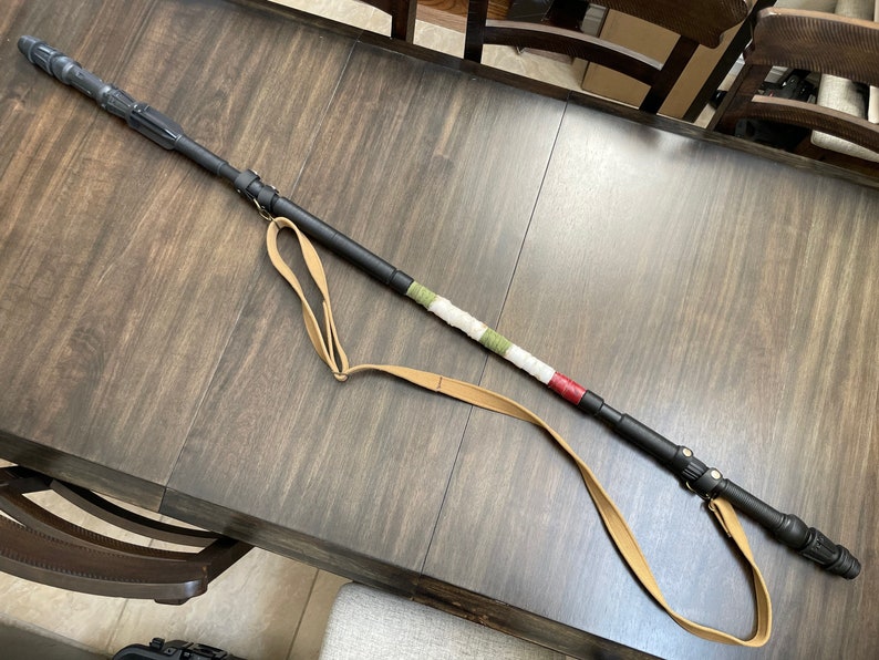 May include: A black walking stick with a brown leather strap and a green, white and red striped section.