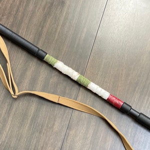 May include: A black telescopic walking stick with a brown leather strap and a white, green and red fabric wrap.
