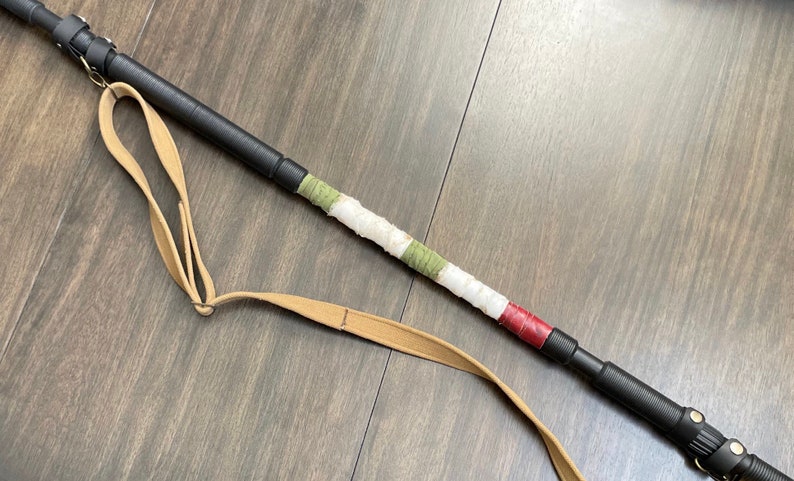 May include: A black telescopic walking stick with a brown leather strap and a white, green and red fabric wrap.