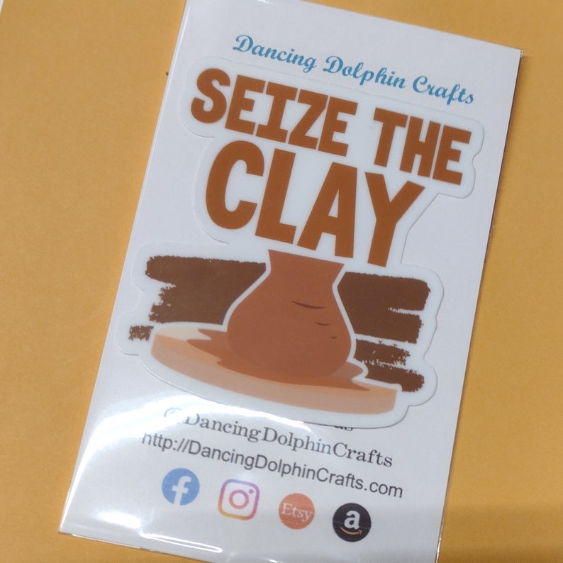 K&ouml;nnte beinhalten: Wei&szlig;er Aufkleber mit dem Text "SEIZE THE CLAY" in braunen Buchstaben. Ein brauner Tontopf steht auf einer braunen Oberfl&auml;che mit wei&szlig;em Hintergrund. Der Aufkleber ist von Dancing Dolphin Crafts.