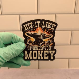 May include: Black and white sticker with a cartoon anvil on fire. The text reads "Hit it like it owes you money".