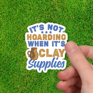 May include: A white sticker with blue and gold text that reads "It's not hoarding when it's clay supplies". A brown clay pitcher is pictured next to the text.
