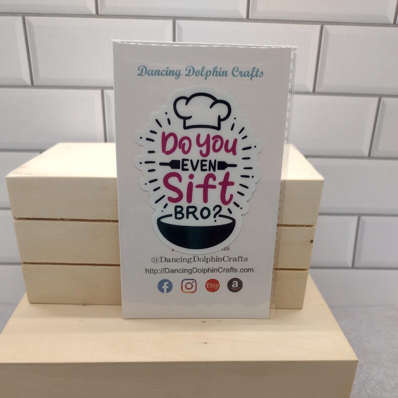May include: White card with a black and white sticker that says "Do you even sift bro?" with a chef's hat and a rolling pin. The sticker is on a white background with black text that says "Dancing Dolphin Crafts" and a website address.