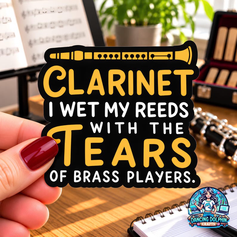 May include: A black die-cut sticker featuring a yellow graphic of a clarinet at the top and the white and yellow text: CLARINET I WET MY REEDS WITH THE TEARS OF BRASS PLAYERS. The sticker has a smooth finish and a distinct, bold, and legible font.