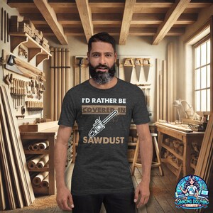 K&ouml;nnte beinhalten: Ein dunkel-melierter grauer T-Shirt mit einem abgenutzten Grafikdruck einer Kettens&auml;ge und dem Text "I'd rather be covered in sawdust".
