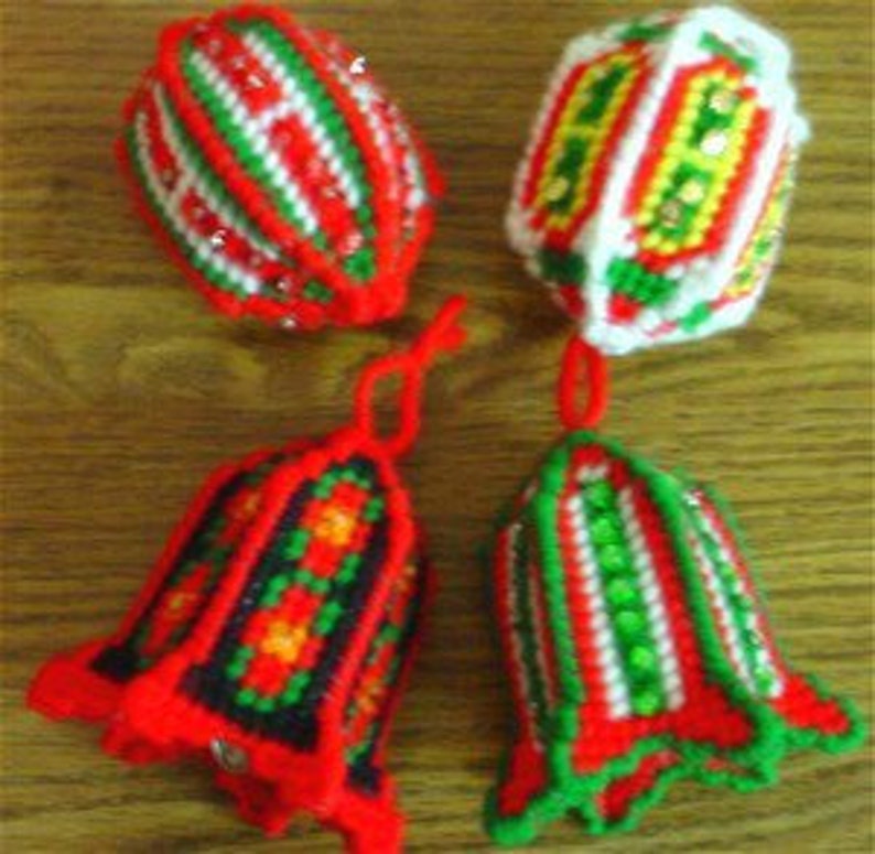 May include: Four handmade plastic canvas ornaments featuring festive red, green, white, and yellow yarn stitching. Two ornaments are bell-shaped with hanging loops, while the other two are rounded, spherical shapes with intricate geometric patterns.