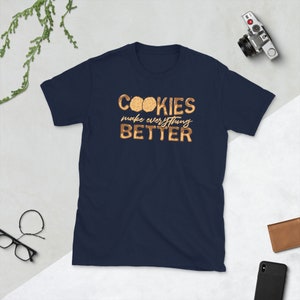 May include: A navy blue t-shirt with the text "COOKIES make everything BETTER" in gold lettering. The text is surrounded by images of chocolate chip cookies.