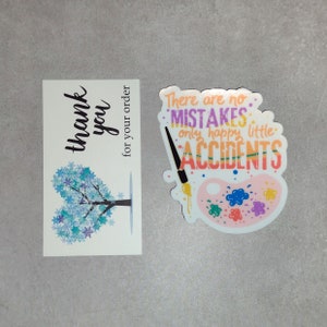 Puede incluir: Una tarjeta de agradecimiento con un dise&ntilde;o de &aacute;rbol de copo de nieve azul y el texto "gracias por su pedido". Una pegatina con una paleta de pintura y el texto "No hay errores, solo peque&ntilde;os accidentes felices" en rosa, morado y verde.